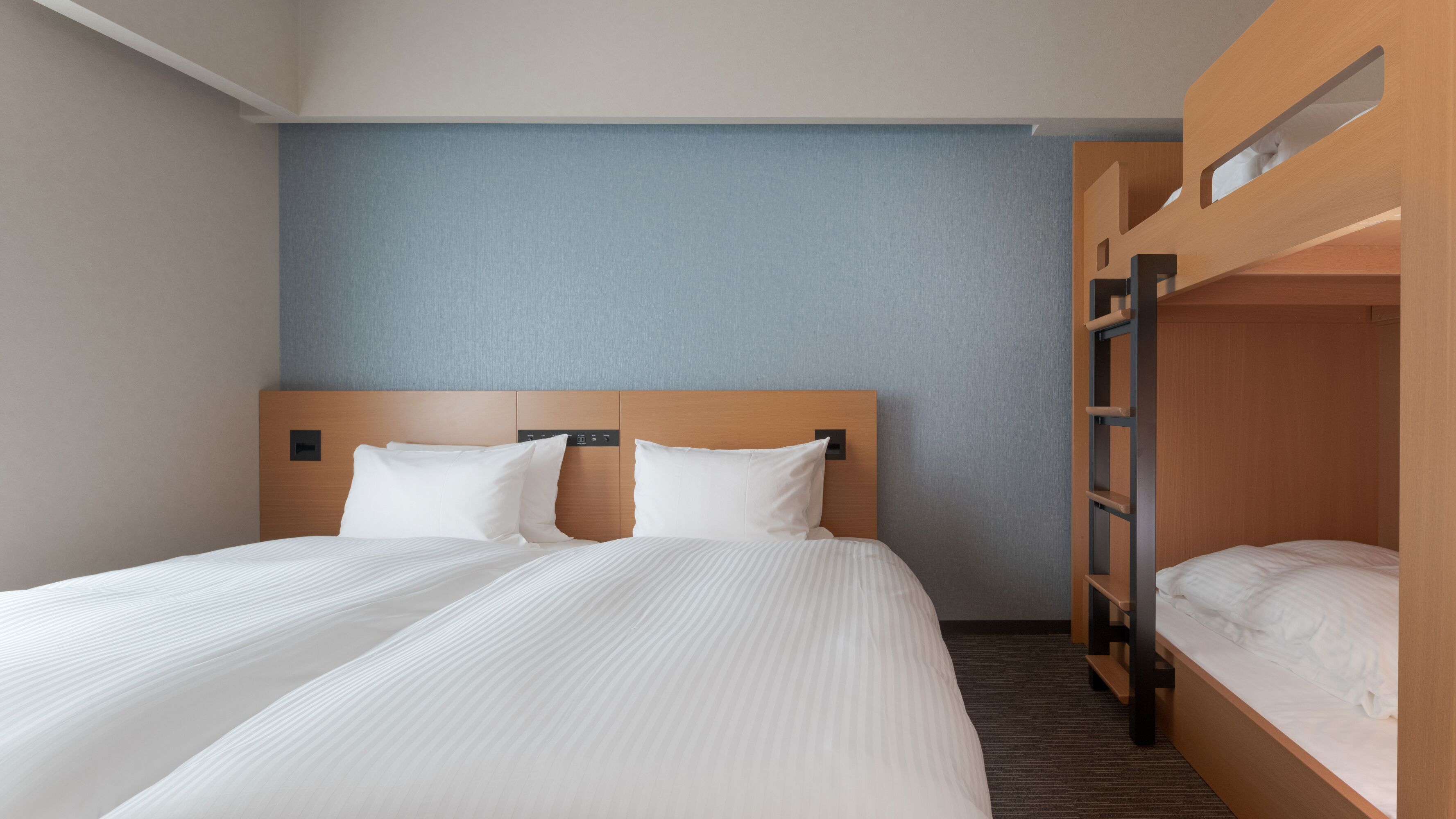A hotel room with a large bed, a bunk bed, and a blue wall.