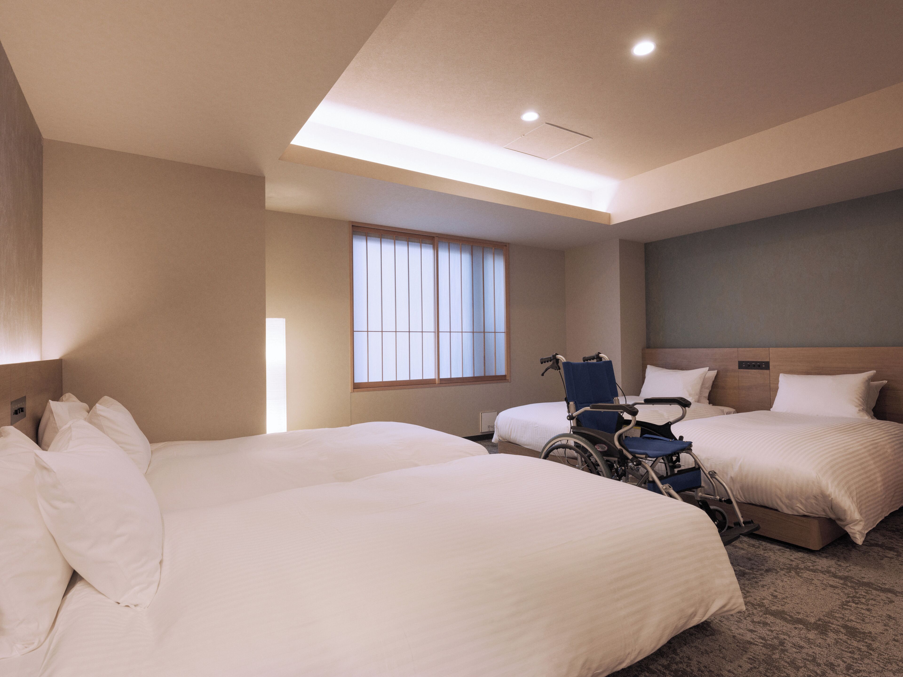 A hotel room with two beds, a wheelchair, and a large window.