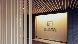 A modern hotel entrance with a sign for 'MIMARU APARTMENT HOTEL' and a slatted ceiling design.
