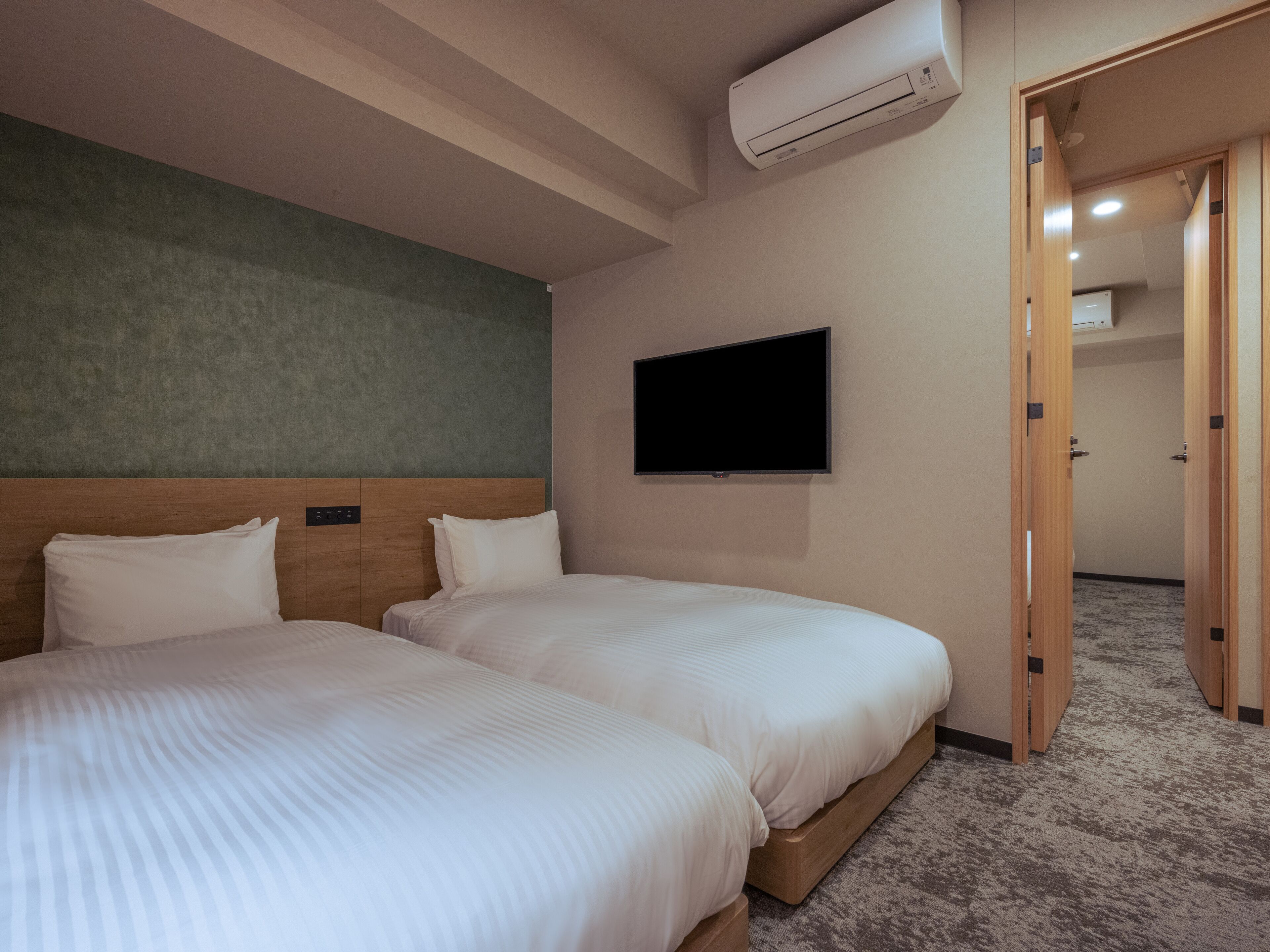 A hotel room with two beds, a flat-screen TV mounted on the wall, and an air conditioning unit above the beds.