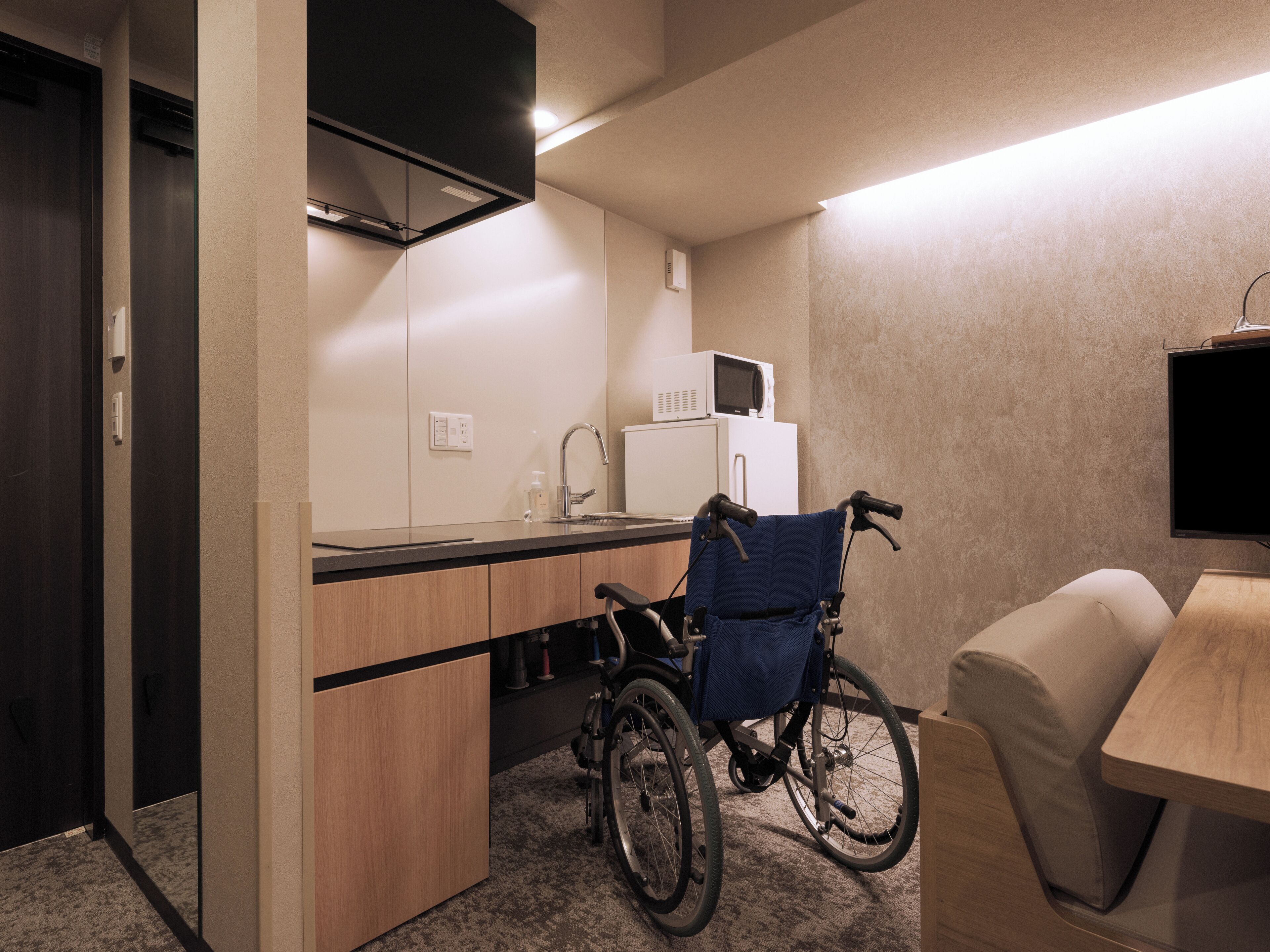 Une petite cuisine équipée d’un four à micro-ondes, d’un évier et de placards. Un fauteuil roulant est garé près du comptoir.