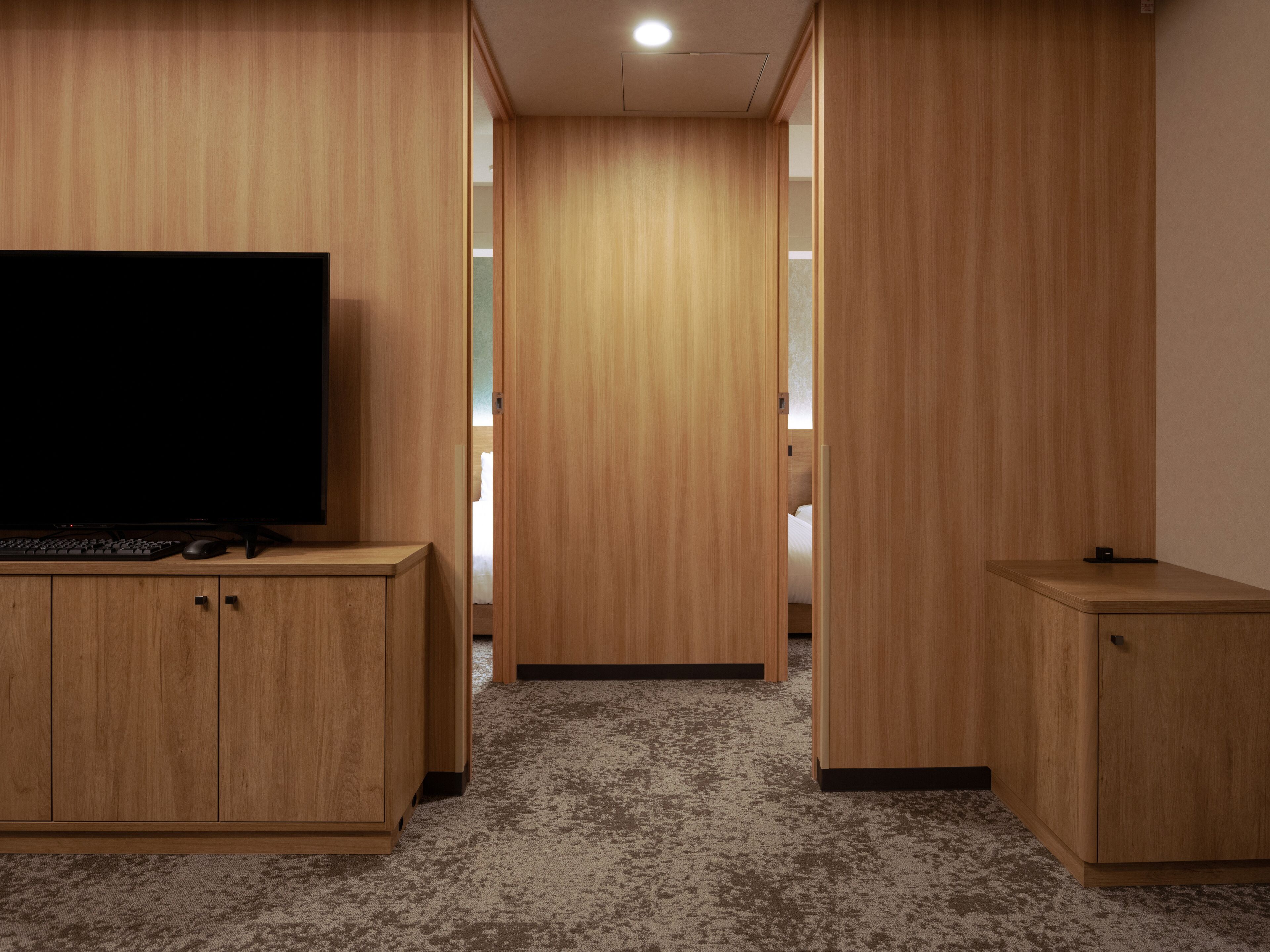 Una habitación con televisión de pantalla plana sobre un escritorio de madera, piso alfombrado y paredes de madera.