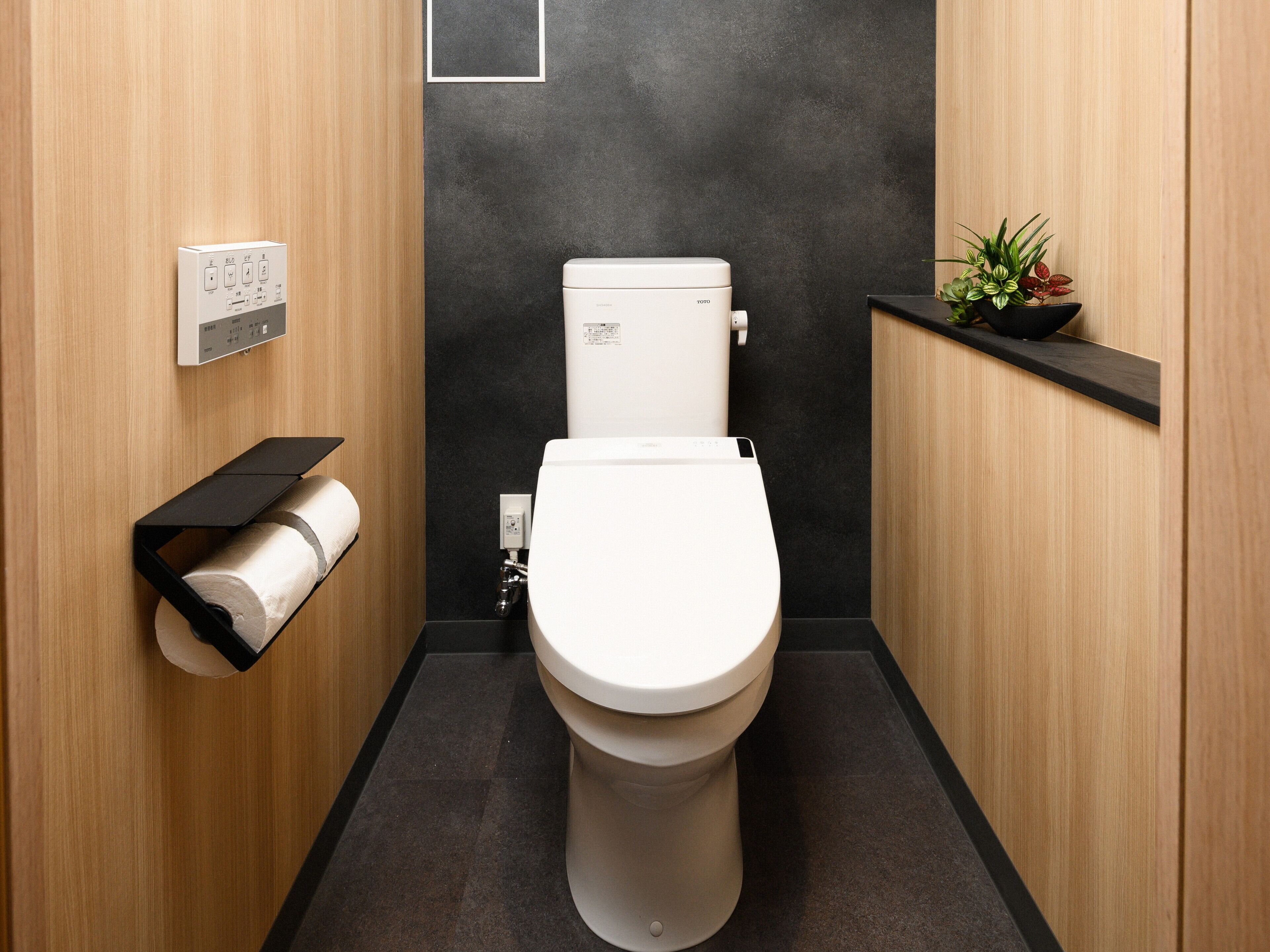 A modern bathroom with a toilet, a toilet paper holder, and a small plant on a shelf.