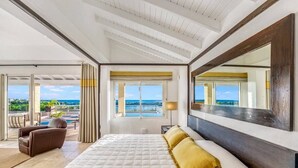 A spacious bedroom with a large bed, a view of the sea, and a balcony with outdoor seating.