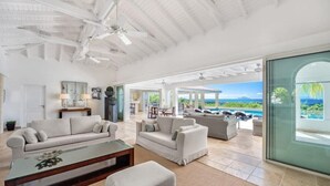 A spacious living room with white sofas, a glass coffee table, and a view of the ocean through large windows.