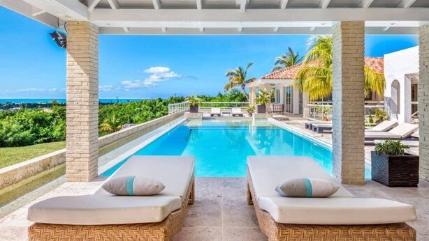 A poolside area with two lounge chairs, a clear view of the ocean, and a pool.