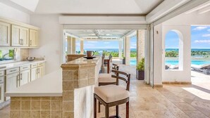 A kitchen with a stone island and bar seating, leading to a patio with a view of the ocean.