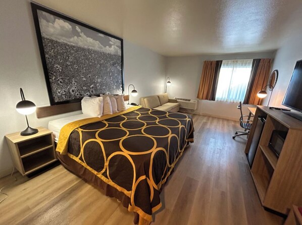 A hotel room with a large bed, a desk, a TV, and a large framed picture on the wall. - Super 8 By Wyndham Sterling CO (Sterling)