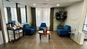 A modern hotel room with a large window, a seating area with two blue sofas, a small round table, and a minibar. - Super 8 By Wyndham Sterling CO (Sterling)