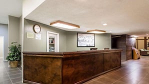 A reception area with a wooden reception desk, a clock, a framed picture, and a small plant. - Super 8 By Wyndham Sterling CO (Sterling)