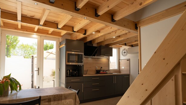 A modern kitchen with wooden beams, a dining area with a table and chairs, and a view of the outside.