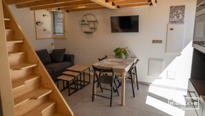 A modern kitchen with wooden beams, a dining area with a table and chairs, a sofa, and a staircase.