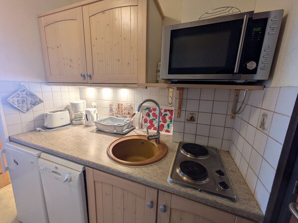 Une cuisine avec des meubles de rangement en bois, un four à micro-ondes, un évier, un grille-pain et un égouttoir à vaisselle.