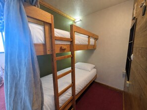 A bunk bed room with a wooden headboard, a small shelf, and a red carpet.