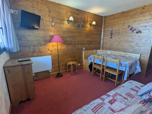 A wooden room with a bed, a desk, a lamp, and a television.