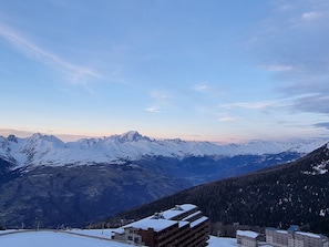 Une chaîne de montagnes enneigée, sous un ciel dégagé. On y voit des bâtiments à plusieurs étages, dotés d’un toit plat, qui font probablement partie d’un hôtel ou d’un complexe touristique.