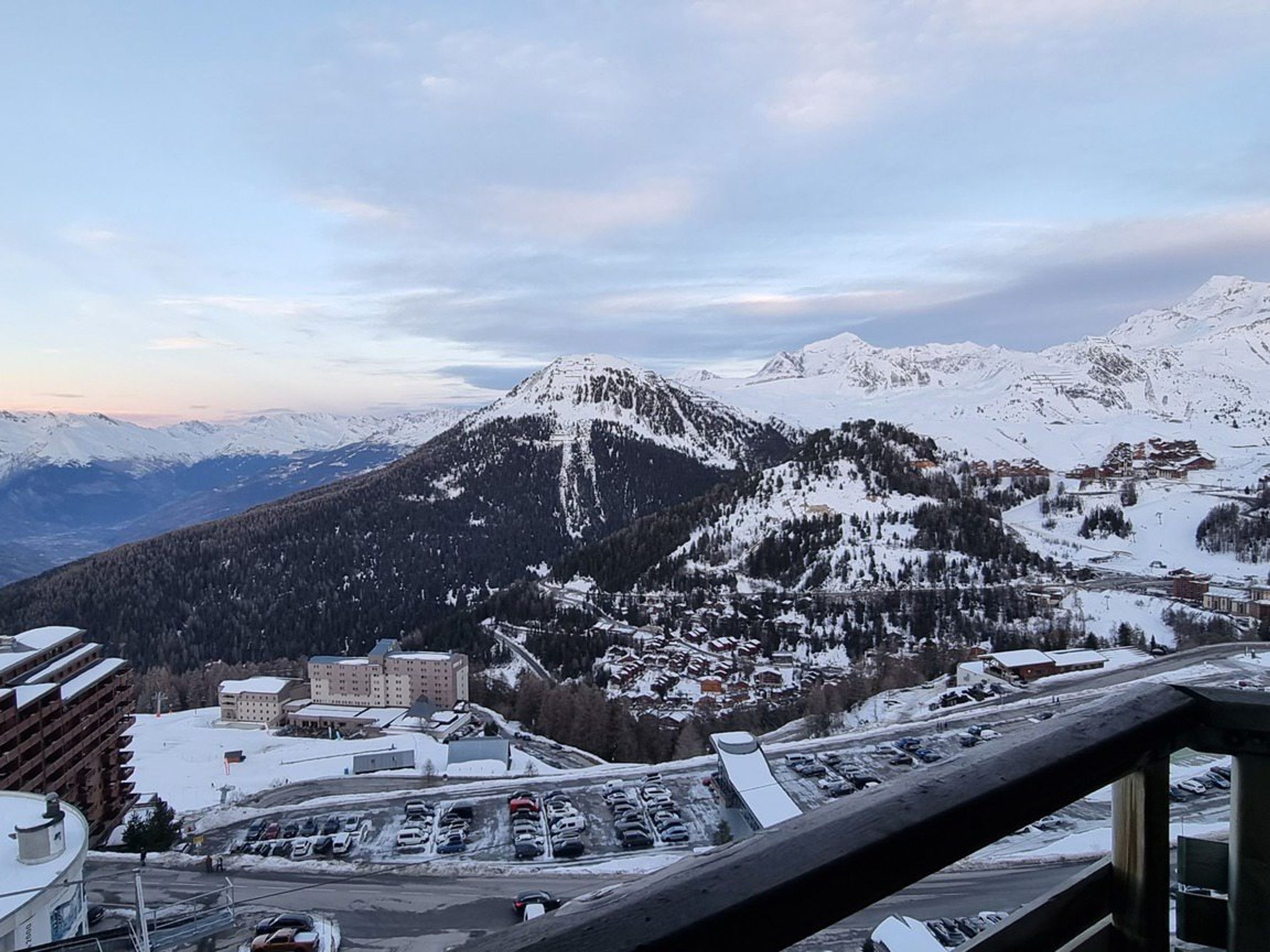 A mountain town with snow-covered peaks, a parking lot, and buildings with a mix of modern and traditional architecture.