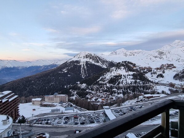 A mountain town with snow-covered peaks, a parking lot, and buildings with a mix of modern and traditional architecture.
