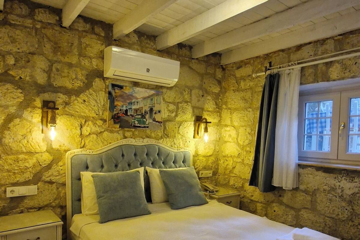 Ein Schlafzimmer mit Stehwand, einem Bett mit Kopfteil, einem Nachttisch, einer Wand-Klimaanlage und einem Fenster mit Vorhängen.