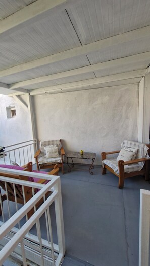 Un espace extérieur abrité, aménagé avec deux chaises en bois, une petite table et une rambarde blanche.