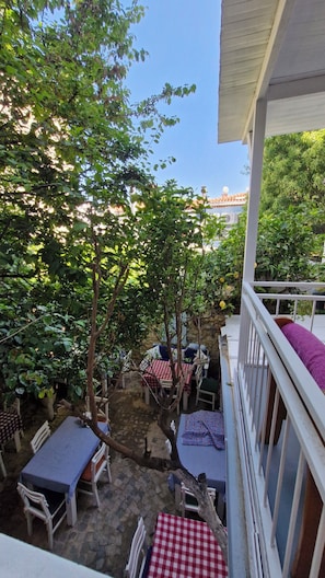 A patio area with tables and chairs, surrounded by trees and a stone wall. - Kaktushan Otel (Cesme)