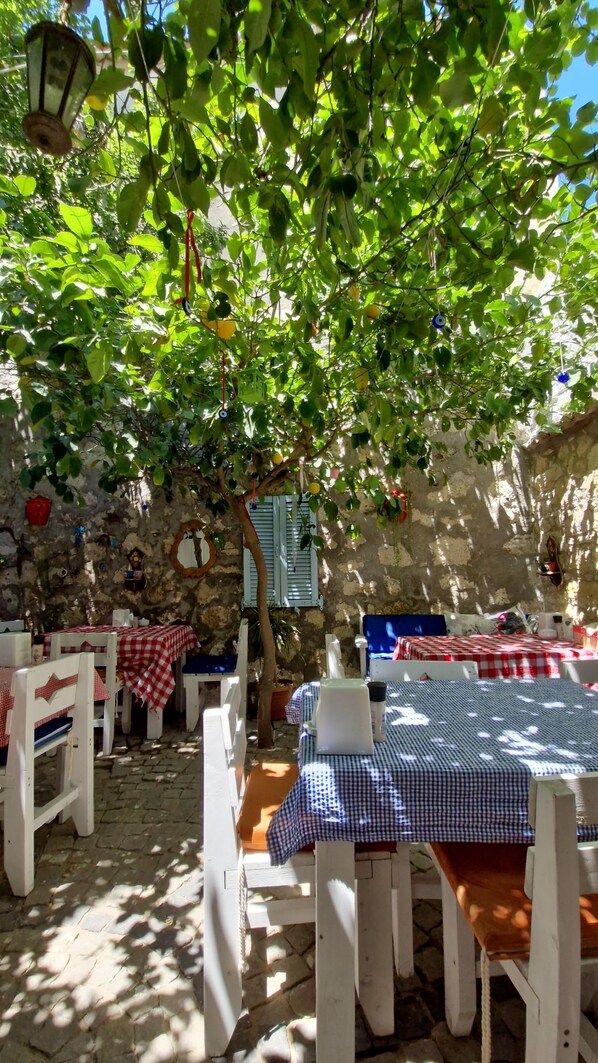 Un espace extérieur aménagé avec des tables et des chaises, un mur en pierre et un arbre qui offre de l’ombre.