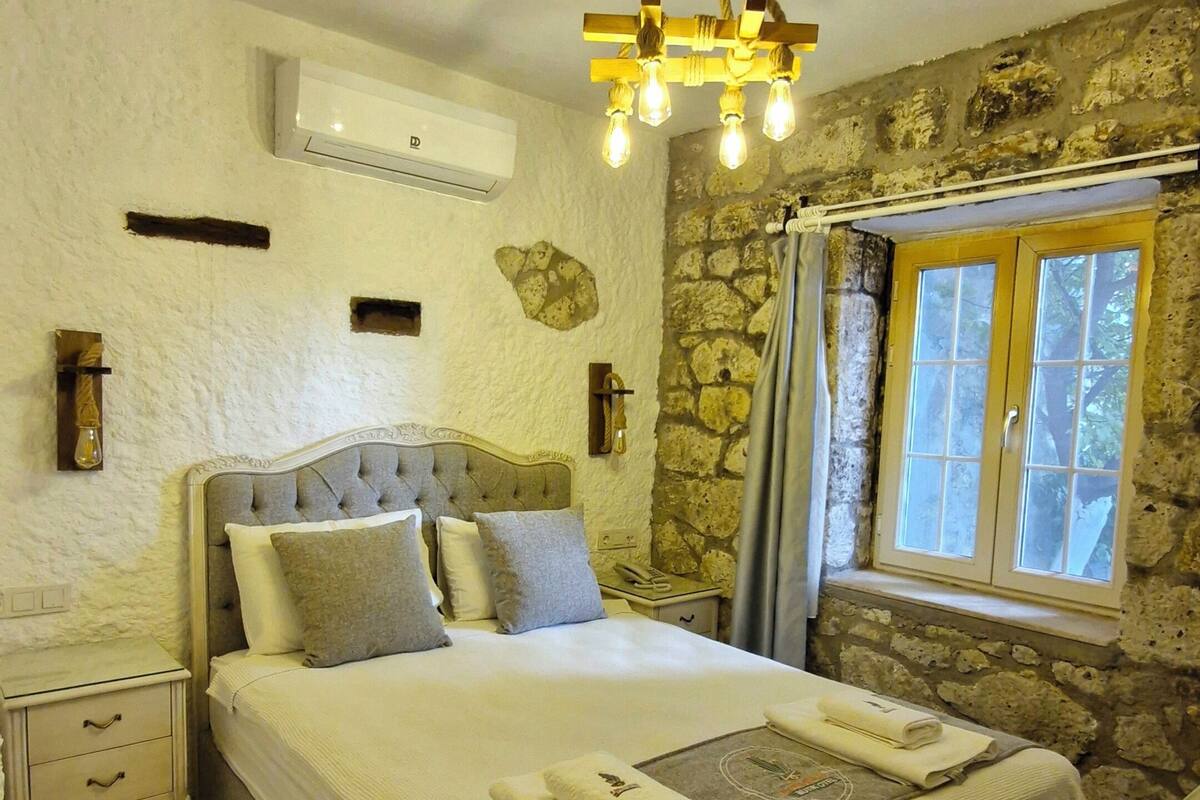 Ein Schlafzimmer mit Bett, Nachttischen, einer Pendelleuchte, einer Steinwand und einem Fenster mit Vorhängen.