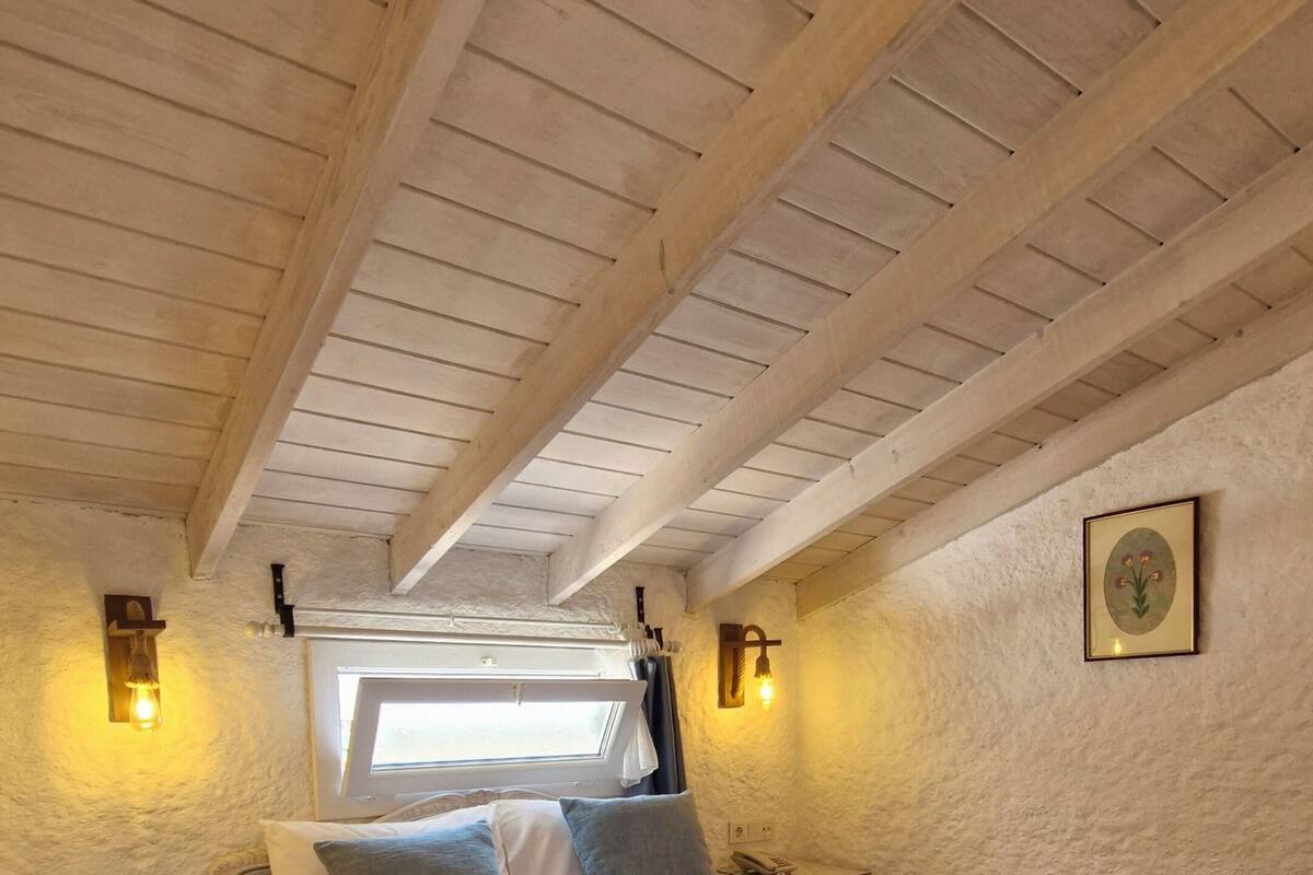Ein Schlafzimmer mit Holzboden, einem Bett mit blauer Decke, zwei Nachttischen und einem Fenster mit Vorhängen.