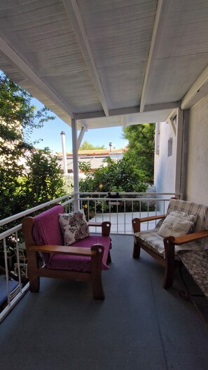 A covered balcony with two wooden chairs and a purple sofa, a railing, and a view of buildings and trees. - Kaktushan Otel (Cesme)