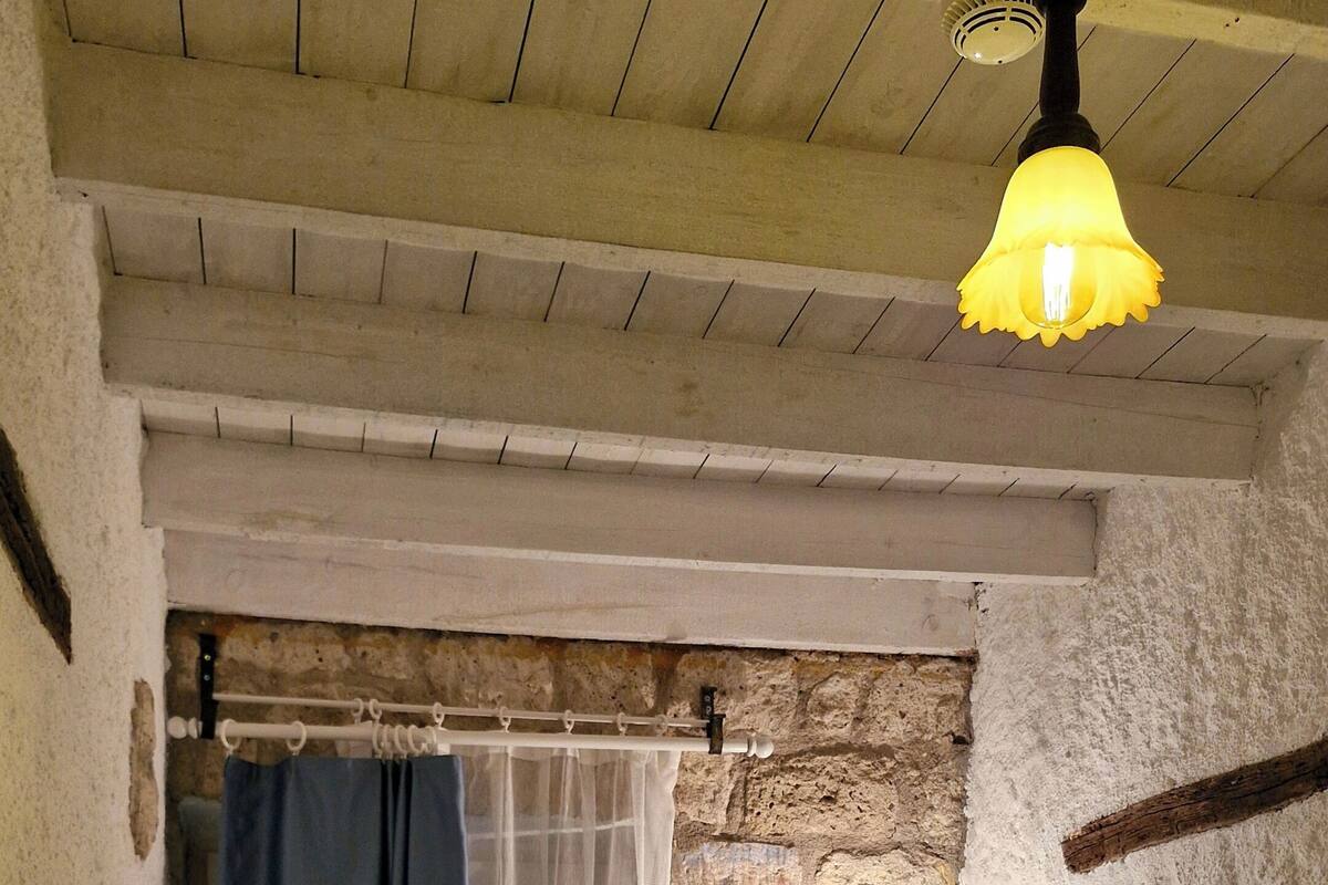 Ein Schlafzimmer mit Bett, Nachttischtelefon, Wandlampe und einem Fenster mit Vorhängen.