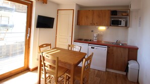 A compact kitchen with wooden cabinets, a microwave, a dishwasher, and a small dining table with chairs.