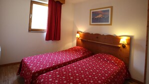 A room with two beds, a window with red curtains, a wall-mounted picture, and two bedside lamps.