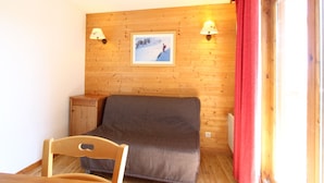 A cozy room with a wooden wall, a bed, a chair, and a table.