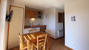 A compact kitchen with wooden cabinets, a microwave, and a sink. There is a dining table with chairs.
