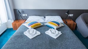 A neatly made bed with white pillows and a colorful striped pillow, a bedside table with a lamp, and a grey armchair. - Cilindar Apartments (Zagreb)
