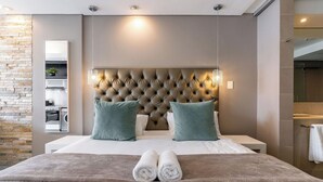 Une chambre d’hôtel moderne dotée d’une tête de lit capitonnée, d’un grand miroir, d’un lave-linge intégré et donnant sur la salle de bain.