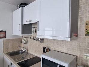 Una cocina con armarios blancos, un fregadero de acero inoxidable y un microondas.