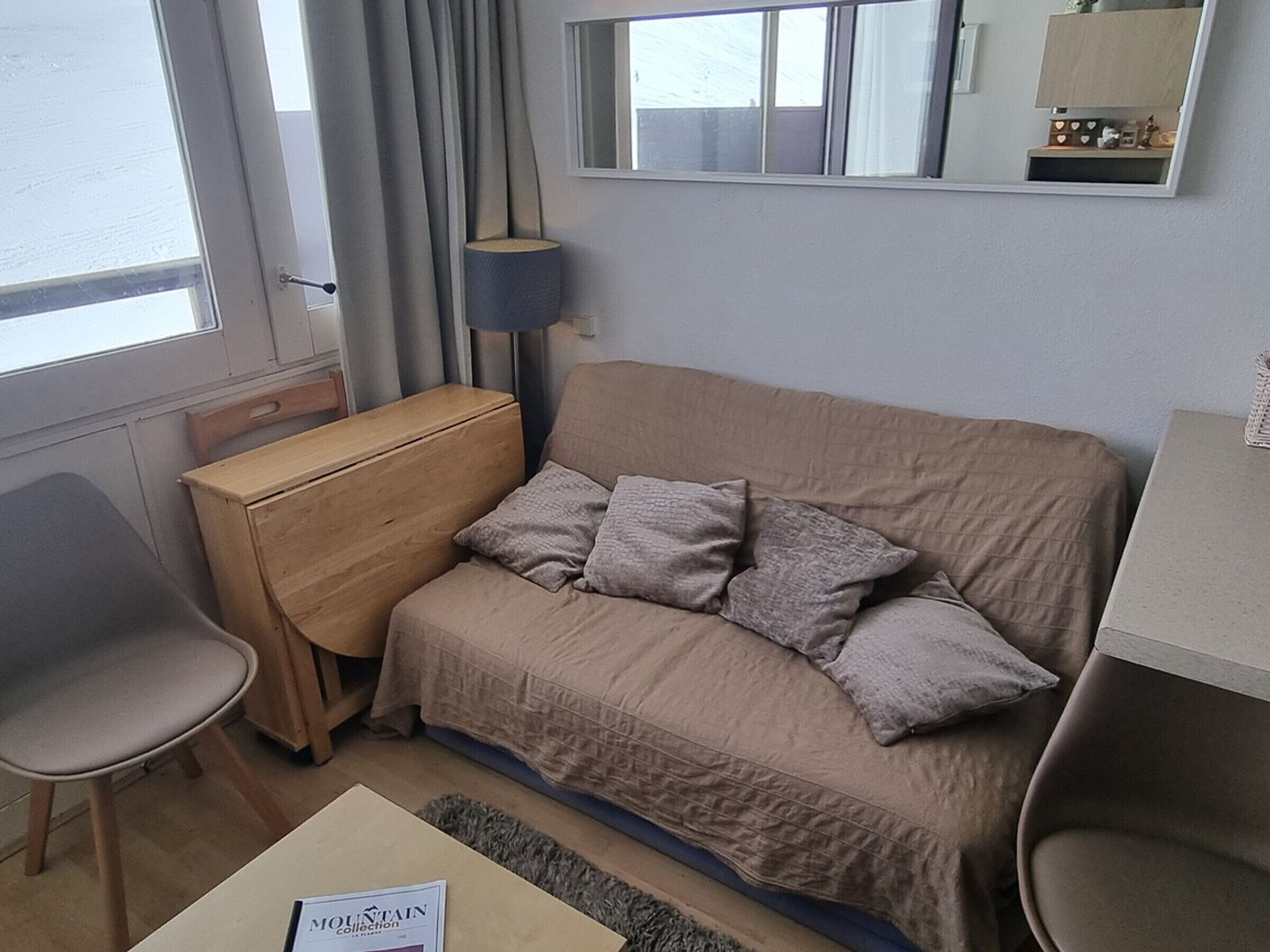 A small, compact room with a sofa, a wooden chest of drawers, a desk, and a chair.