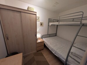 A compact room with a bunk bed, a wardrobe, a bedside table with a lamp, and a framed picture on the wall.