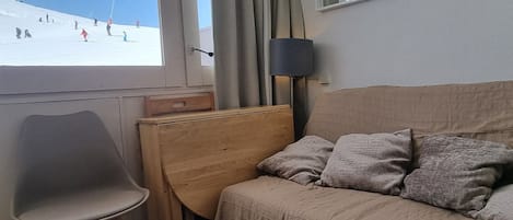 Une chambre d’hôtel avec un lit, une chaise, une table et une fenêtre donnant sur un paysage enneigé.