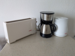 A kitchenette with a toaster, a coffee maker, and a white appliance, possibly a rice cooker, on a countertop.