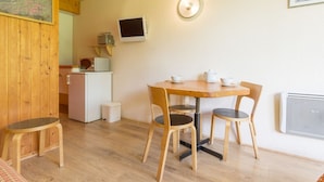 A cozy room with a wooden dining table and chairs, a small kitchenette, and a television mounted on the wall.