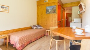 A small, cozy room with a wooden bunk bed, a wooden dining table with chairs, a small kitchenette, and a television mounted on the wall.