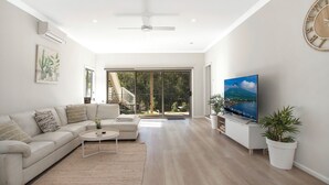 A spacious living room with a large TV, a sofa, a coffee table, and a staircase leading to a balcony. - Fully renovated coastal retreat- beach escape (Umina Beach)
