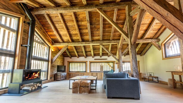 A spacious loft with exposed wooden beams, a fireplace, large windows, and a cozy seating area. - Detached 500m2 Farmhouse with Yoga Studio, Hot Tub and Sauna (Samoëns)