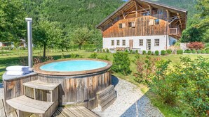A wooden chalet with a hot tub and deck, surrounded by lush greenery and mountains. - Detached 500m2 Farmhouse with Yoga Studio, Hot Tub and Sauna (Samoëns)