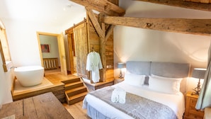 A bedroom with a large bed, a wooden staircase, a white bathtub, and a wooden table. - Detached 500m2 Farmhouse with Yoga Studio, Hot Tub and Sauna (Samoëns)