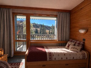 A wooden room with a bed, a window with a view of a mountain, and a wooden wall.