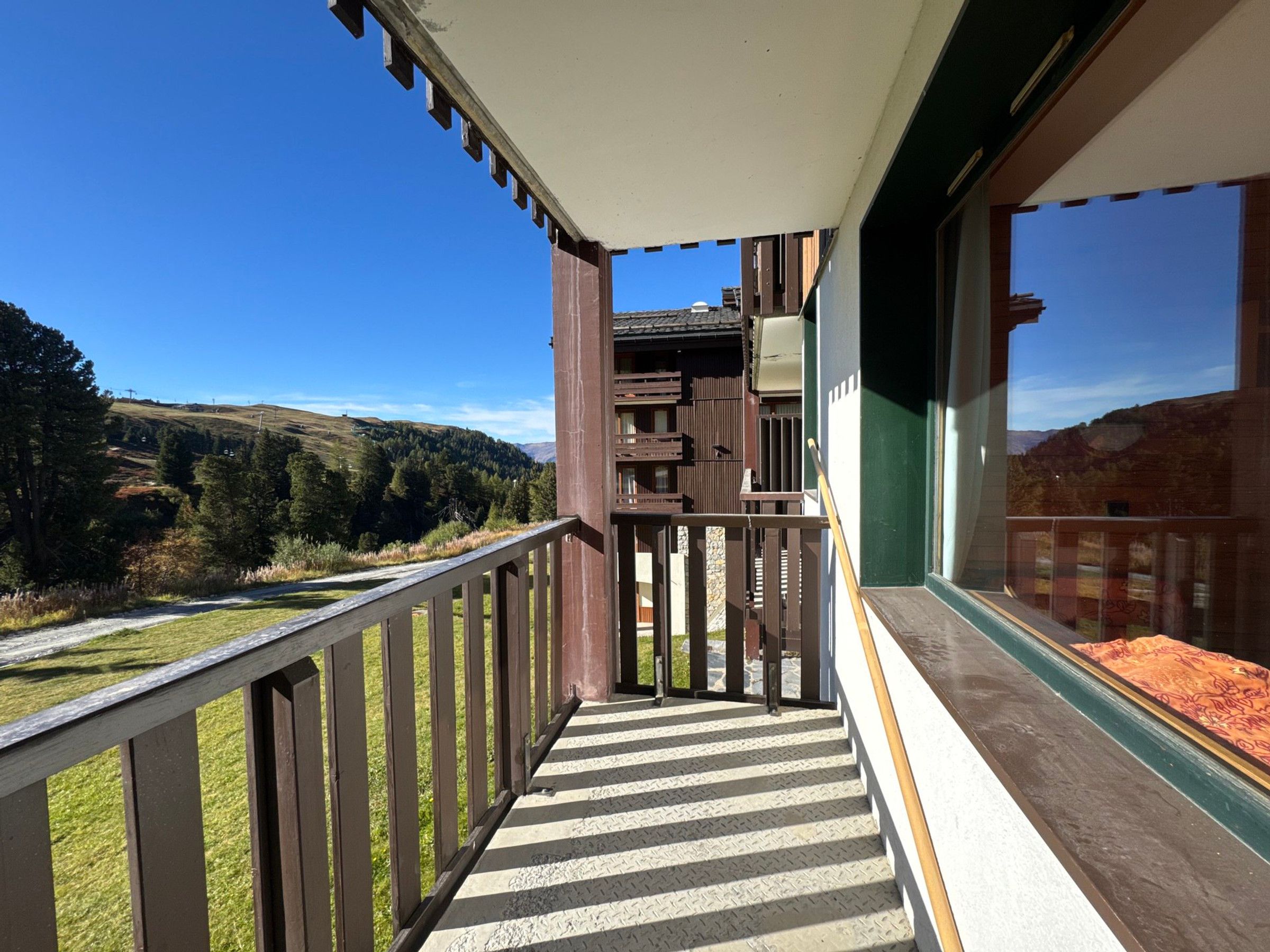 A balcony with a view of a hilly landscape, a wooden railing, and a door leading to an interior space.
