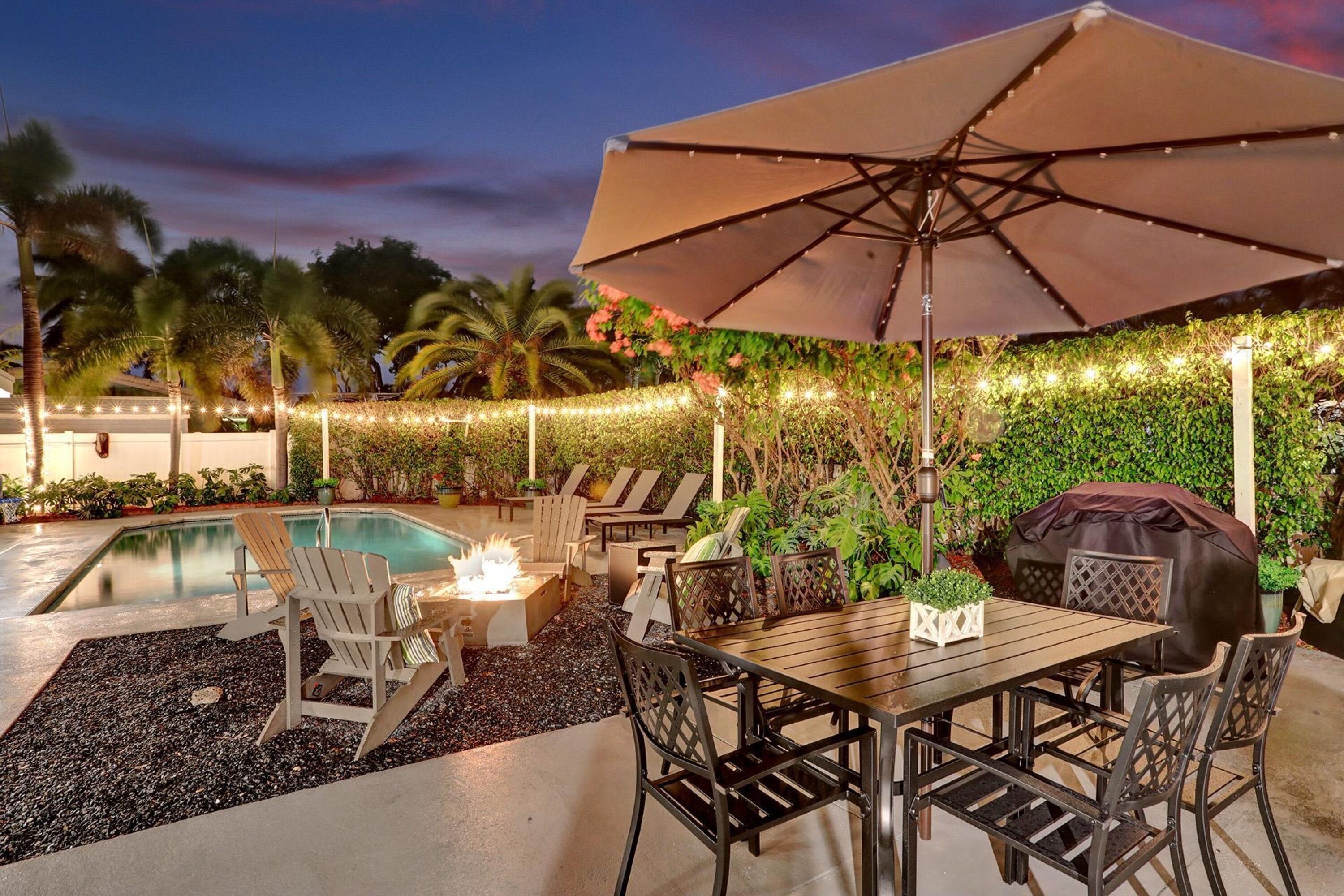 Un patio exterior con piscina, sillas de descanso, una mesa y una sombrilla.